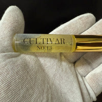 Gold tube labeled 'Cultivar No. 13' held in a white gloved hand against a black background