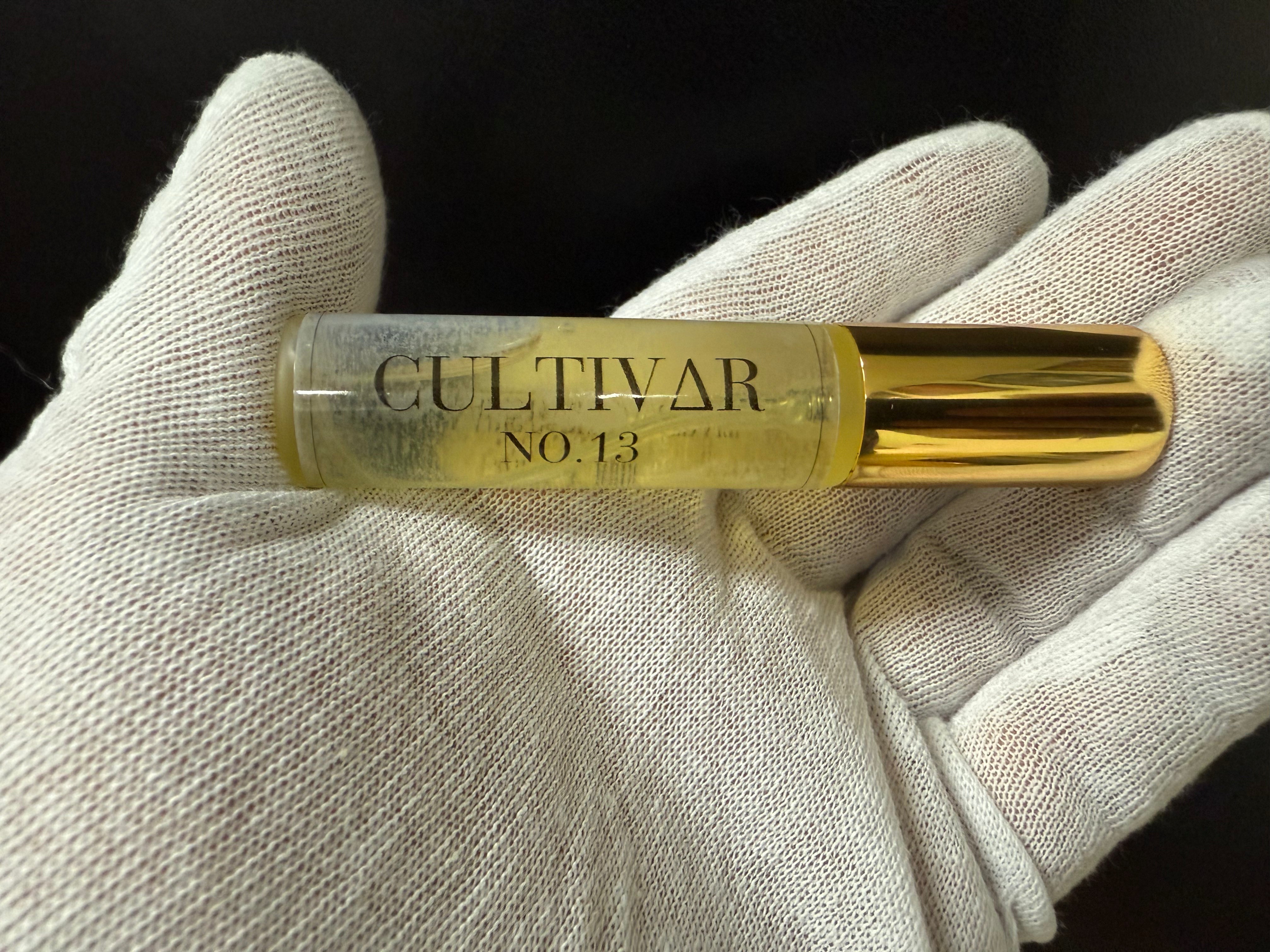 Gold tube labeled 'Cultivar No. 13' held in a white gloved hand against a black background
